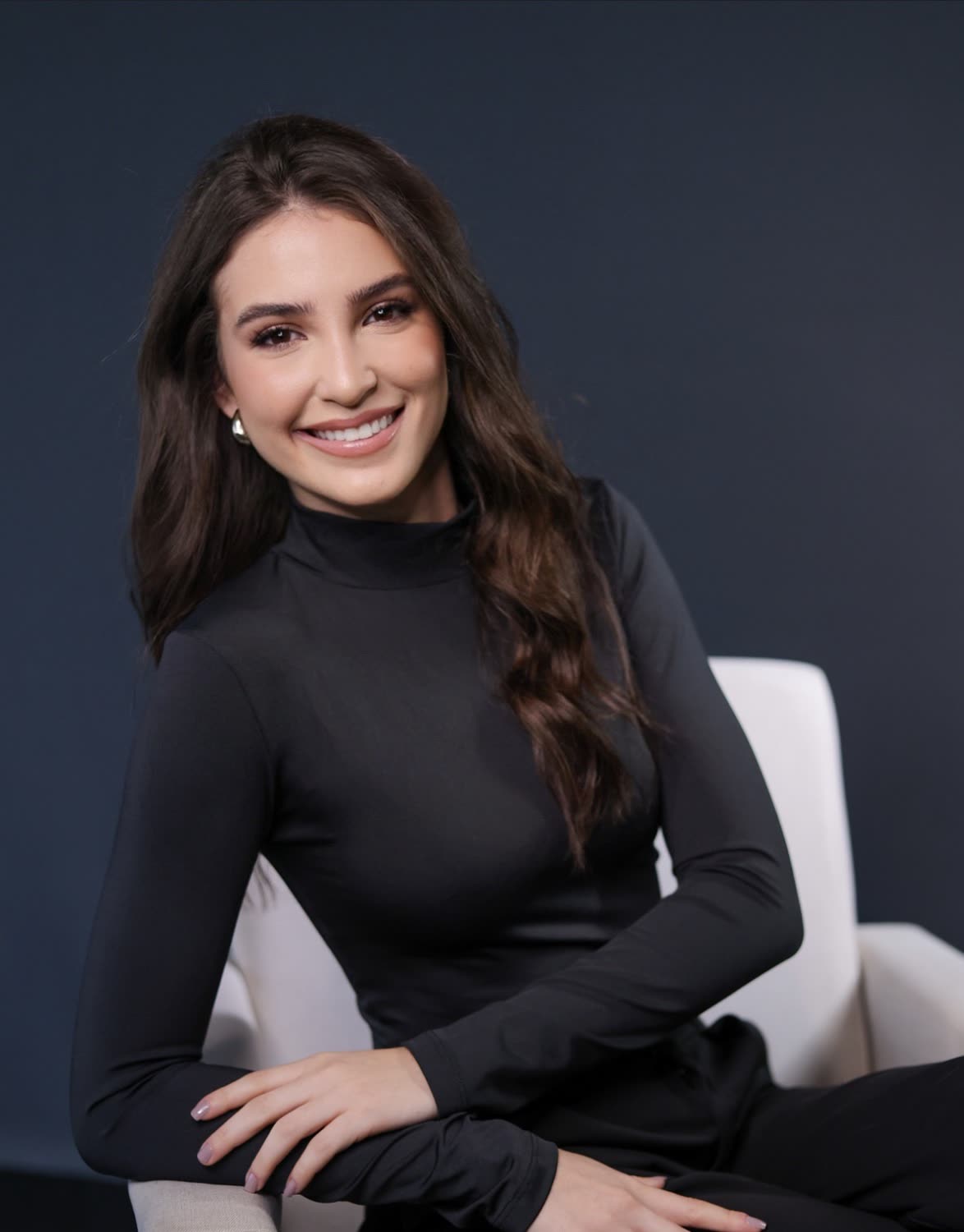 Dra. Rafaela Bergamin sorrindo, de blusa preta, sentada numa poltrona clara